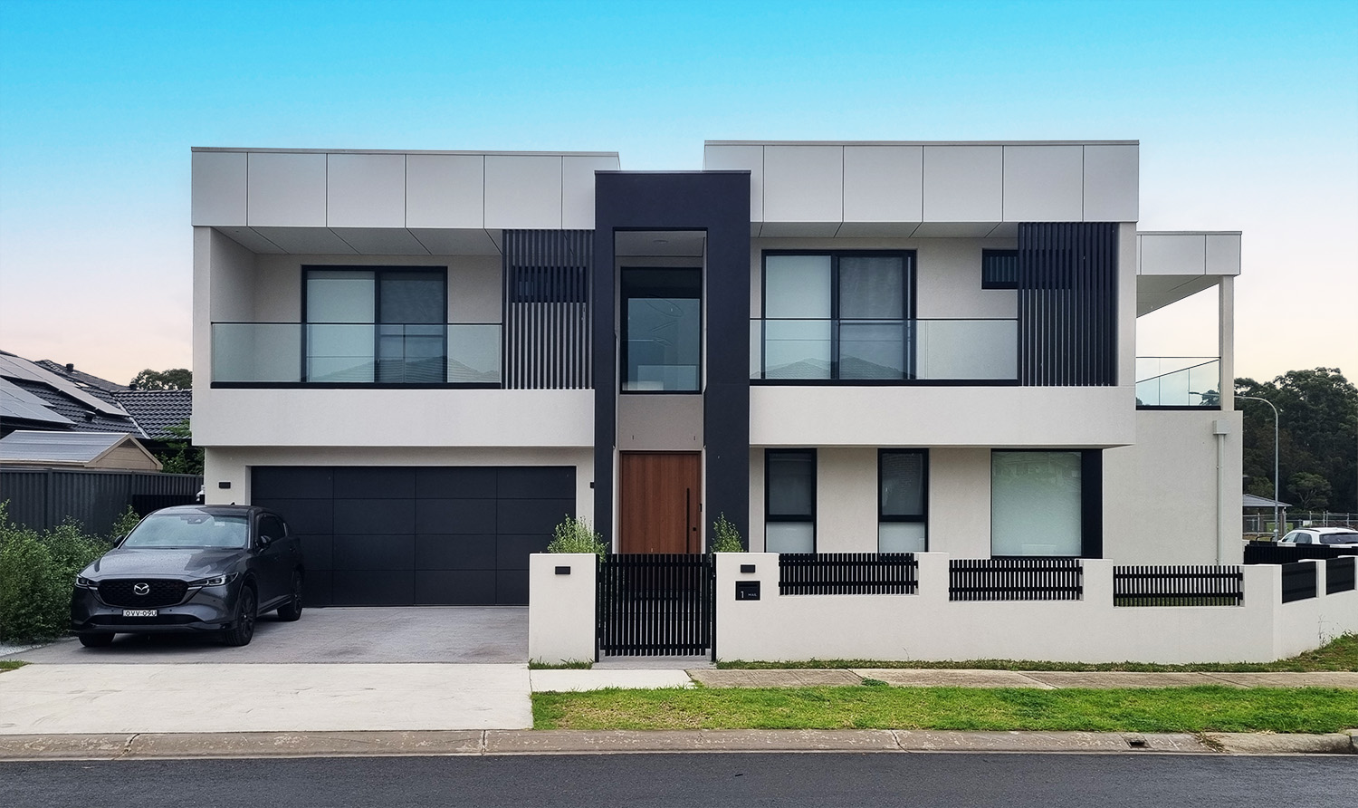 Photograph of the completed Edmondson Park house, white render with dark vertical entry feature and timber front door